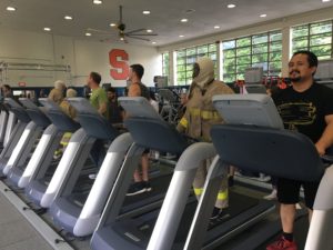 Persons are walking on treadmills 3 of them are in fire outfits