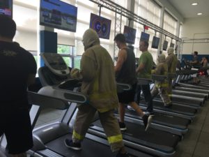6 persons are walking on treadmills 3 wear fire suits