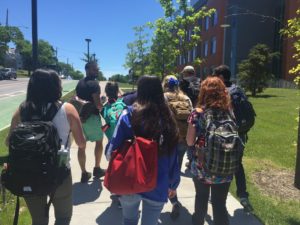 8 persons with backpacks are walking down a sidewalk at Syracuse University