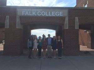 7 persons are posed in front of the entrance to Falk College