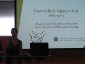 A women gives a presentation a slide behind her says "How to best support our veterans..."