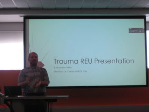 A man presents with a slide behind him saying "Trauma REU Presentation"