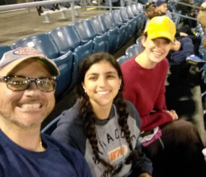 3 persons are posed in a baseball stadium during a game