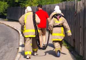 3 persons in fire outfits walk with another in street clothing