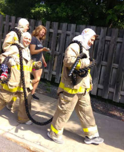 3 persons in fire suits are walking and carrying a heavy rope