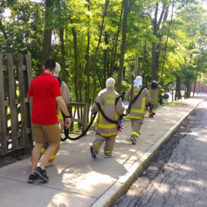 3 persons in fire suits carry a heavy rope down a side walk with another in normal street clothes